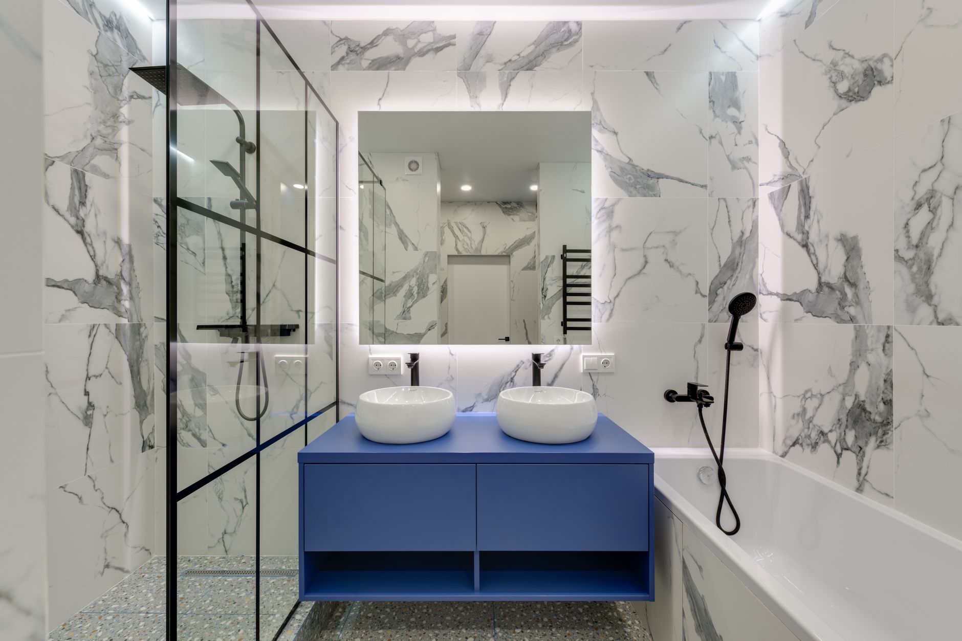 Modern bathroom interior featuring marble walls, dual sinks, and a glass shower in Lakewood, CA